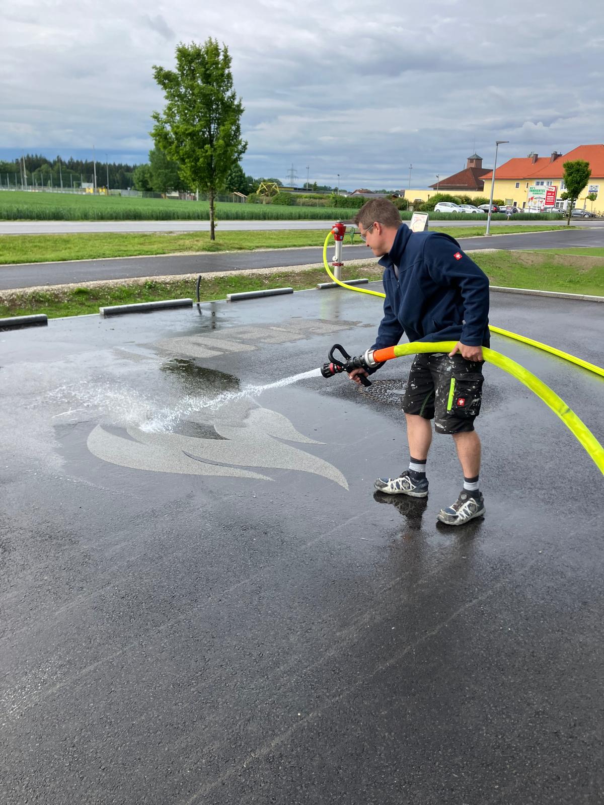 Mann mit Feuerwehrschlauch wäscht Split weg